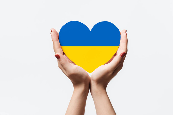 Women hands holding ukraine flag color heart shape paper on white background. - Photo, Image