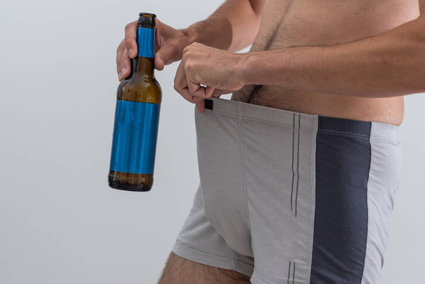 a man in underwear is holding a bottle of beer. - Фото, изображение