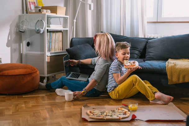 mother and son sitting on floor in living room and eating pizza - Fotoğraf, Görsel