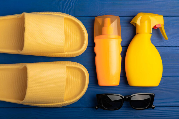 Flat lay composition with beach accessories on blue texture background. Beach slippers,sunglasses and sunscreen.SPF sun protection.Space for copy.Place for text.Vacation concept. - Foto, Imagen