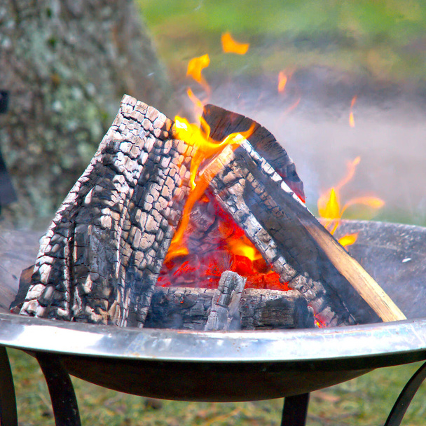 A closeup of a small bonfire with burned wood pieces in a big metal pot - 写真・画像