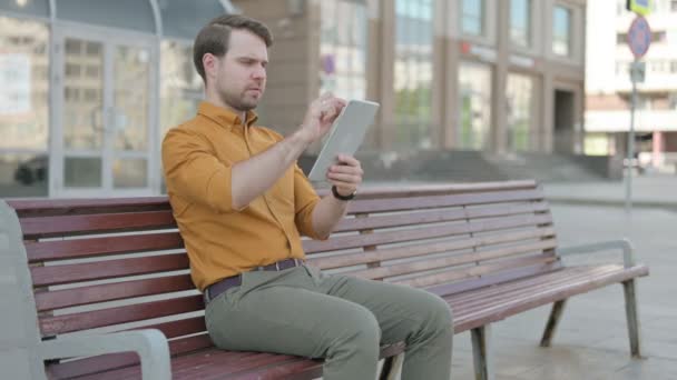 Casual Young Man using Tablet while Sitting Outdoor on Bench - Video