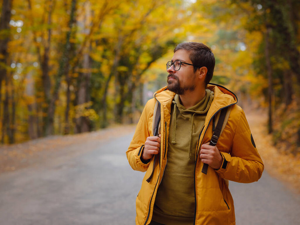 Νεαρός όμορφος άντρας ποζάρει στο φθινόπωρο. νεαρός hipster τύπος με σακίδιο, ταξιδιώτης στέκεται στο δάσος, Πεζοπορία, Δάσος, Ταξίδι, ενεργό υγιεινό τρόπο ζωής, περιπέτεια, διακοπές έννοια. - Φωτογραφία, εικόνα