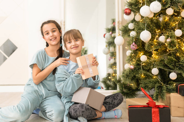 Two cute little girls under Christmas tree. Children under Christmas tree with gift boxes. New Years decorations. Sisters. - Photo, Image