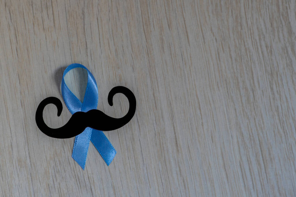 Prostate Cancer Awareness, light Blue Ribbon with mustache on wooden background for supporting people living and illness. Men Healthcare and World cancer day concept - Photo, Image