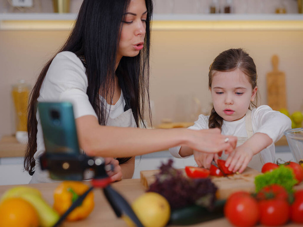 Happy mother and daughter enjoy prepare freshly salad together in kitchen. Healthy food at home. Healthy Lifestyle and Eating Concept. little influencer filming blog about healthy eating - Foto, afbeelding