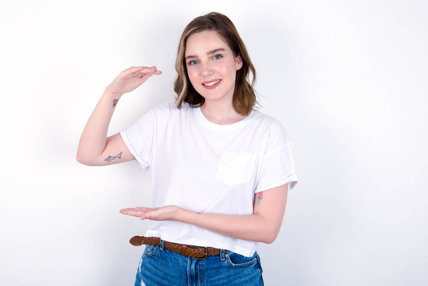 girl gesturing with hands showing big and large size sign, measure symbol. Young caucasian woman wearing white T-shirt over white background  - Photo, Image