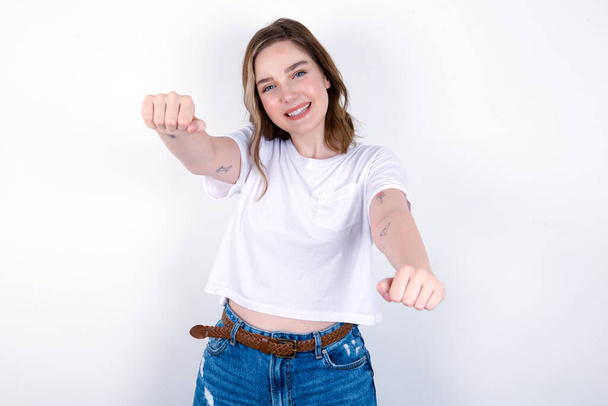 Πορτρέτο του γοητευτικό κορίτσι χαμογελώντας ευρέως, ενώ κρατώντας τα χέρια πάνω από το κεφάλι της. Εμπιστοσύνη και να χαλαρώσετε έννοια. Νεαρή λευκή γυναίκα που φοράει λευκό μπλουζάκι πάνω από λευκό φόντο  - Φωτογραφία, εικόνα