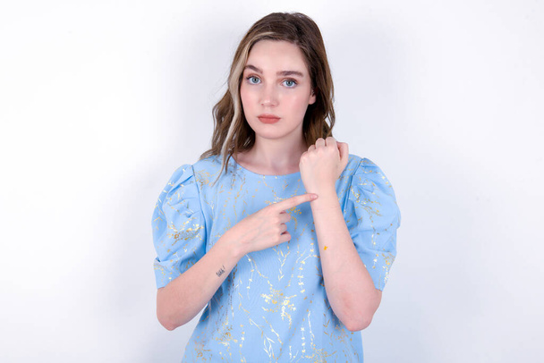 mladá běloška v modrém tričku na bílém pozadí spěšně ukazuje na čas, netrpělivost, rozčilená a rozzlobená kvůli zpoždění termínu - Fotografie, Obrázek