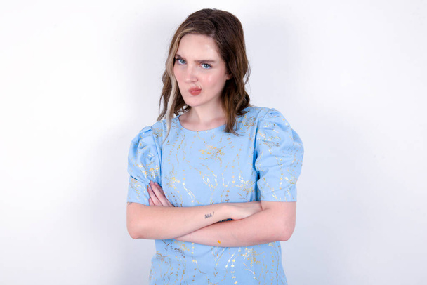 Immagine di una giovane donna caucasica arrabbiata che indossa una maglietta blu su uno sfondo bianco incrociando le braccia. Guardando la fotocamera con espressione delusa. - Foto, immagini