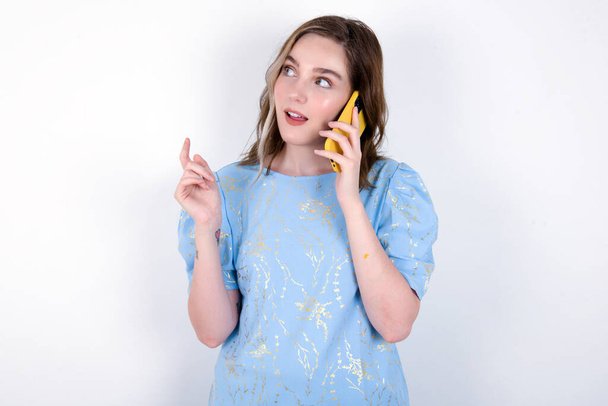 giovane donna caucasica che indossa blu T-shirt su sfondo bianco parla al telefono cellulare  - Foto, immagini