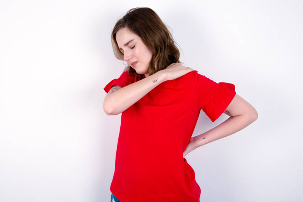 νεαρή καυκάσια γυναίκα φορώντας κόκκινο T-shirt πάνω από λευκό φόντο πήρε πόνο στην πλάτη - Φωτογραφία, εικόνα