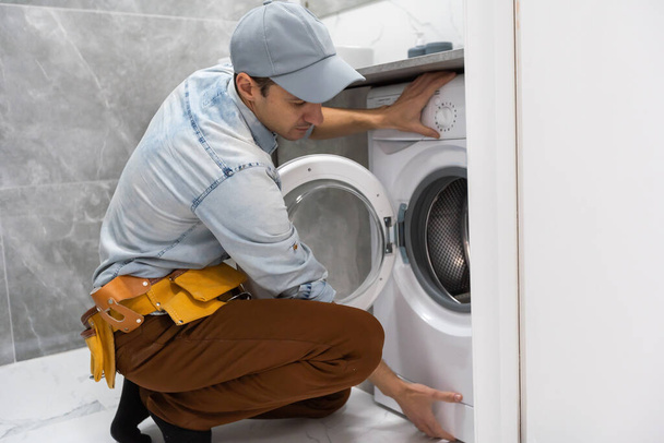 dolgozó ember vízvezeték szerelő javít egy mosógép a mosodában. - Fotó, kép