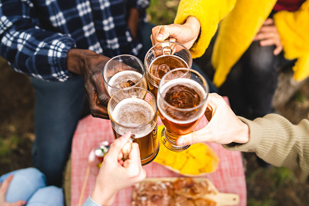 Nahaufnahme multiethnischer Hände, die Bierkrüge halten und gemeinsam im Freien anstoßen - Konzept der multiethnischen Jugendlichen, die sich zum Happy Hour-Trinken treffen - Schwerpunkt auf der Hand der Frau in Gelb - Foto, Bild