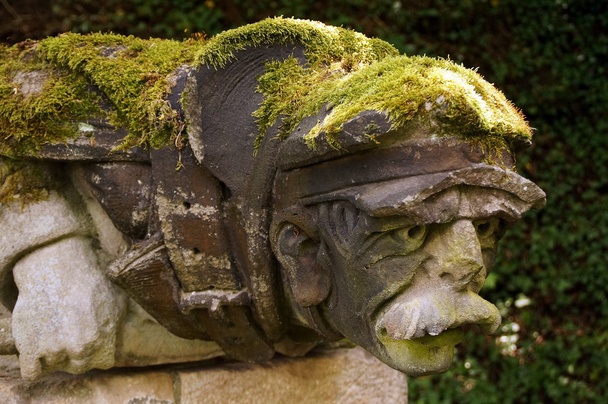 Gargoyles in the form of an old man - the cap and the back overgrown with moss. - Photo, Image