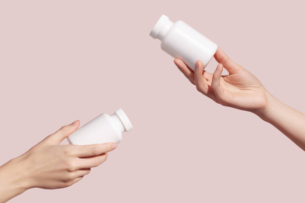 Hands holding blank white plastic tubes on pink background. Packaging for pills, capsules or supplements. Medic product branding mockup. High quality photo - Foto, Bild