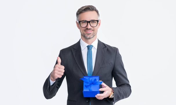mature man in eyeglasses and suit hold present box isolated on white background. thumb up. - 写真・画像