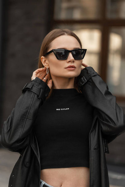 Fashion beauty woman with cool vintage sunglasses in black street fashionable outfit with leather coat and t-shirt walks in the city - Foto, Bild