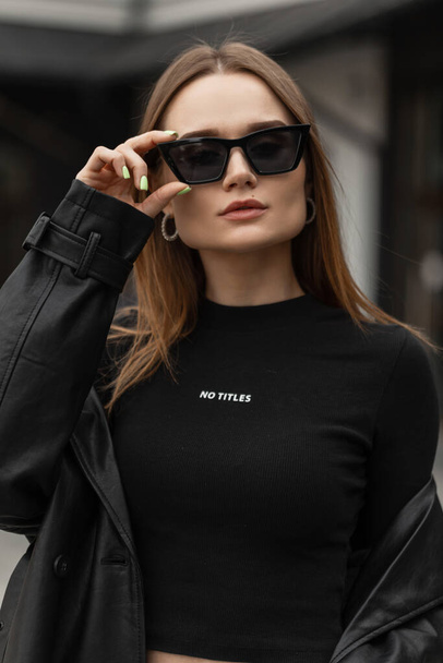 Şık siyah elbiseli güzel bir genç kızın şehir portresi sokakta siyah havalı güneş gözlüğü takıyor. - Fotoğraf, Görsel