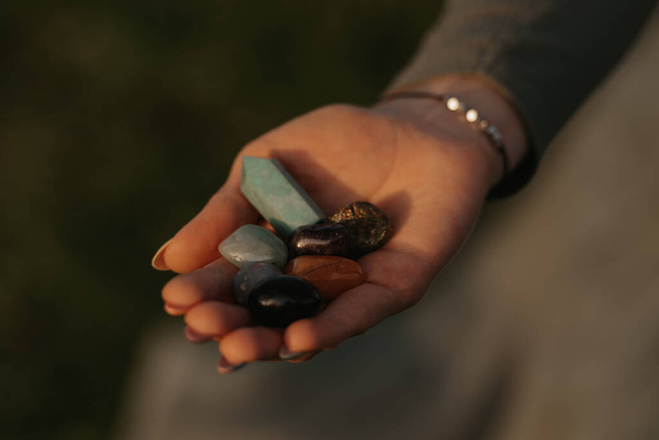 A close photo of a bunch of colorful stones on the hand of a woman for magical therapy. Session of a meditation healing in the park at sunset. - 写真・画像