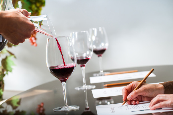 Hand schenkt Rotwein bei Weinprobe ein. - Foto, Bild