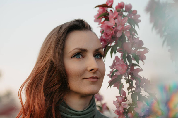 A headshot of a redhead woman is staring into the distance with flowering sakura in the background at sunset. - Foto, Imagem
