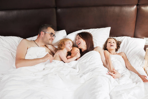 A boldog család otthon fekszik a takaró alatt az ágyban. - Fotó, kép