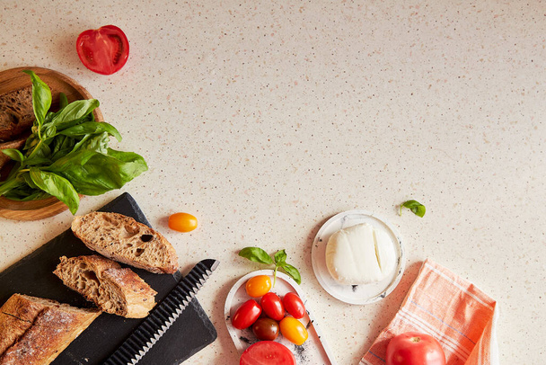 Bereiding van het Italiaanse diner - Caprese salade met verse rode en gele tomaten, mozzarella, basilicum en brood. Bovenaanzicht eten. Rustiek klassiek voorgerecht. Kopieerruimte. - Foto, afbeelding