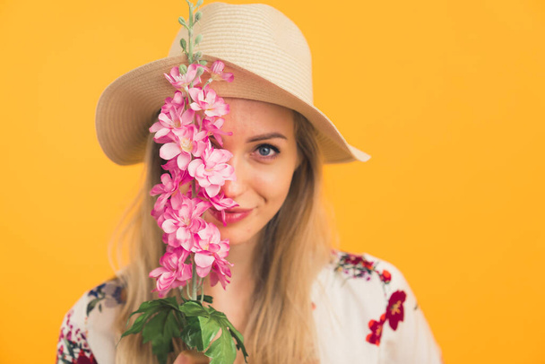 kaukázusi lány kalapban, virággal a kezében, narancssárga háttérrel a kamerába néz. Kiváló minőségű fénykép - Fotó, kép