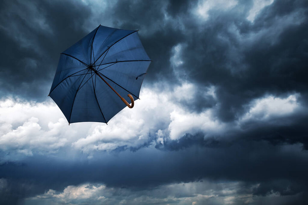 Flying blue umbrella and cloudy rainy sky closeup. Weather forecast concept - Zdjęcie, obraz