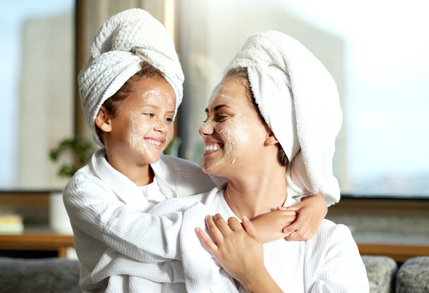 Happy, smiling and relaxed mother and daughter spa day at home with face masks for healthy skincare and personal hygiene. Cute little girl and parent bonding and enjoying a pamper treatment together. - Photo, image
