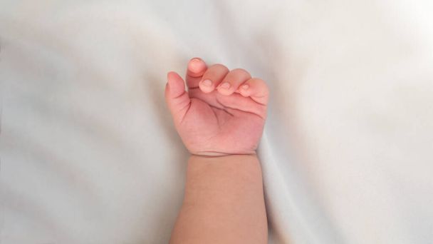 Close up of newborn boy hand on white sheet background. Baby sleeping on the bed. A beautiful conceptual image of childhood. Family and home concept with copy space. - Fotografie, Obrázek