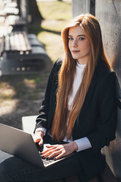 Woman student e-learning on distance remotely on laptop, doing homework, sitting on park bench. Online education. Internet technology. - Foto, Imagem