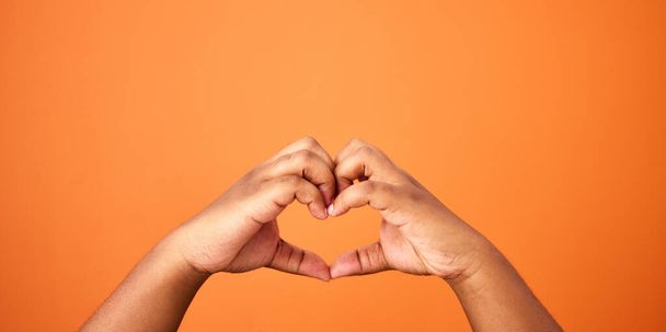 Love is all we need. an unrecognizable person showing a heart gesture against an orange background - Valokuva, kuva