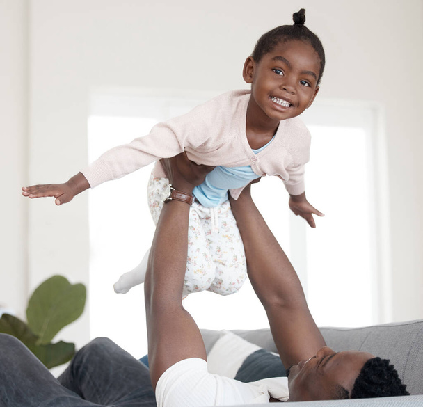 Teach your kids how to fly. Cropped portrait of an adorable little girl playing with her dad on the sofa at home - Фото, изображение
