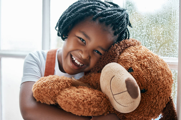 She finds her teddy to be soft and comforting. Portrait of an adorable little girl holding a teddy bear at home - Foto, Bild