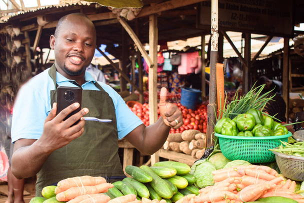 на фото щасливого африканського продуктового продавця з фартухом і смартфоном, готовий продавати клієнтам. - Фото, зображення