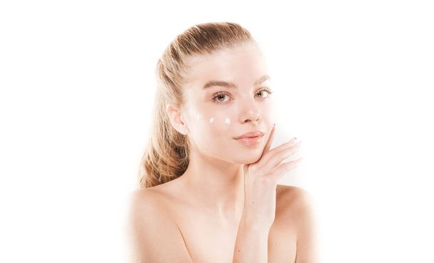 Beautiful young girl with fresh skin is posing and putting some cream on her face in studio on white background. Skin care. Spa - Фото, изображение