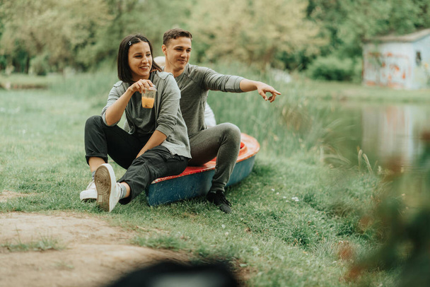 Knappe jongen tonen iets aan zijn vriendin terwijl zitten op hij rode kajak in het park - Foto, afbeelding