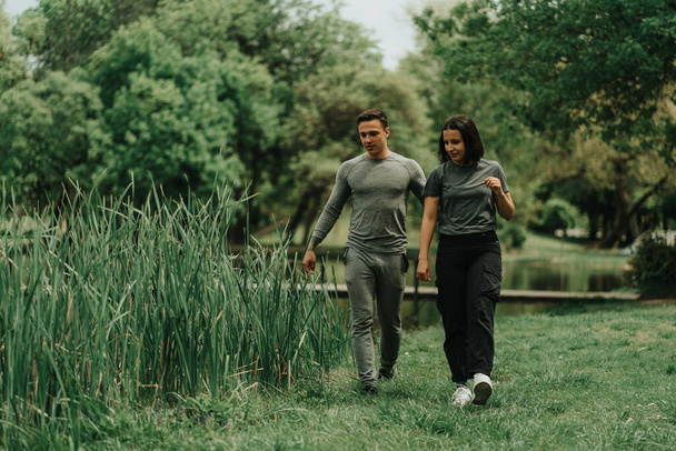 Close up of beautiful sport couple walking in the park and looking for something on the ground near the lake - Foto, imagen