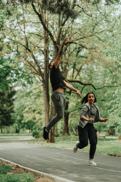 Beautiful couple jumping on the silver path while running in the park - Foto, Imagem