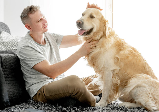 Young handsome man with his golden retriever dog in bright living room. - Foto, Imagem