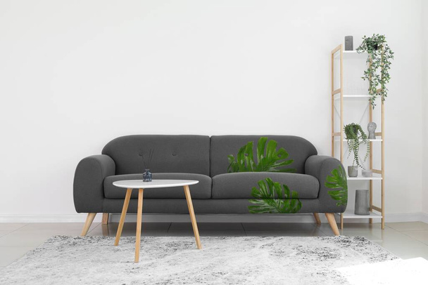 Comfortable sofa with print of monstera leaves, table and shelf unit near light wall in room - Fotoğraf, Görsel