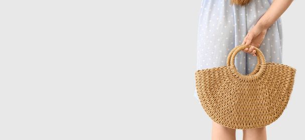 Elegant young woman with rattan bag on light background with space for text, back view - Fotó, kép