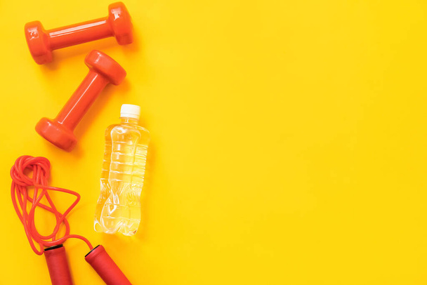 Bottle of water, dumbbells and skipping rope on yellow background - Foto, Imagem