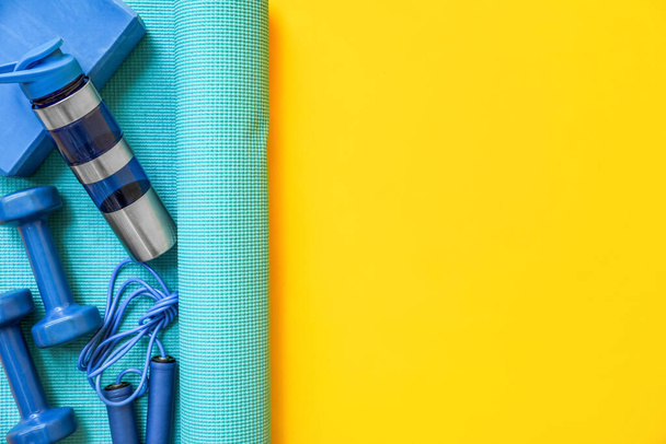 Yoga mat with different sports equipment on yellow background - Zdjęcie, obraz