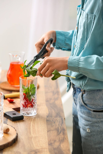 Woman adding fresh mint into glass with strawberry lemonade in kitchen - 写真・画像