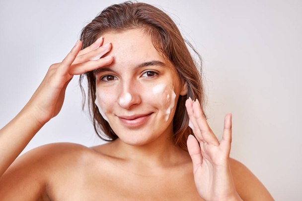 Bir kız cildini temizlemek için yüzüne köpük sürer. Yüz bakımı kavramı. - Fotoğraf, Görsel