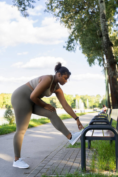 Plus sized African-American woman exercising at the park using a bench in a summer day  - Foto, Bild