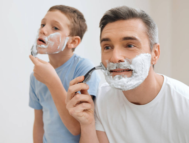 Always go with the grain. a handsome mature man teaching his young son how to shave in the bathroom at home - Zdjęcie, obraz
